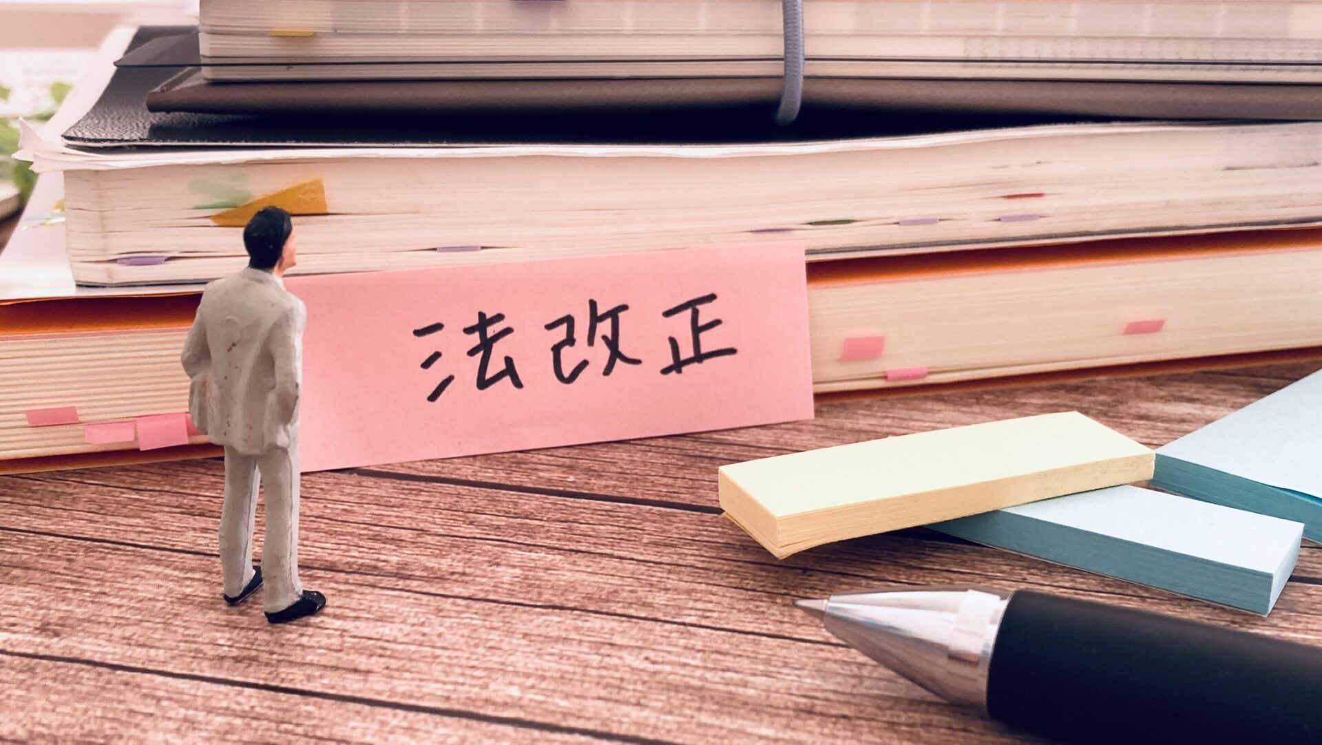 法改正の付箋を見つめるビジネスマンのミニチュア。区分所有法改正と管理規約改定を象徴するイメージ。
